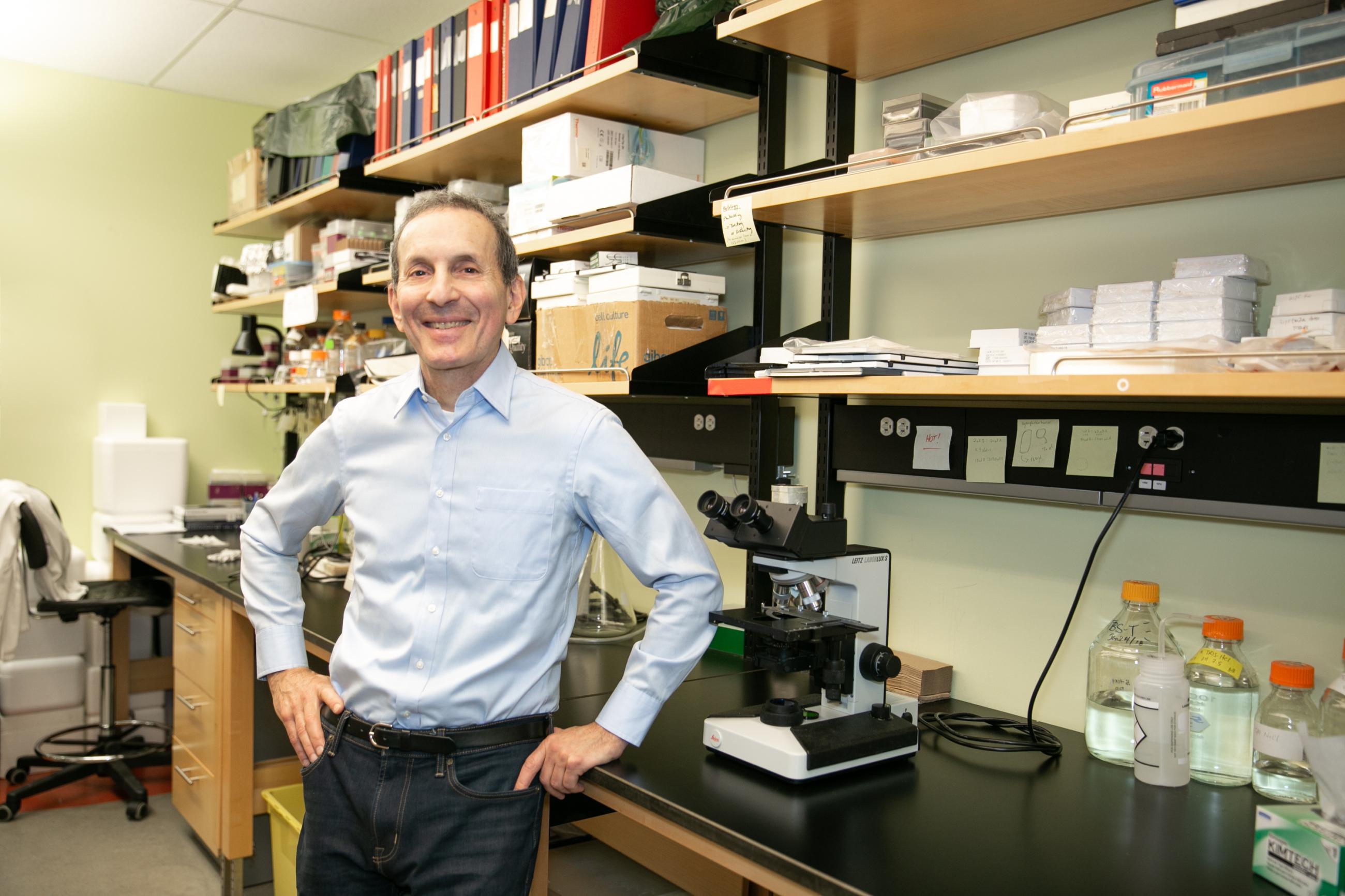 Dr. Daniel Drucker in a light blue dress shirt standing in his lab with a smile.