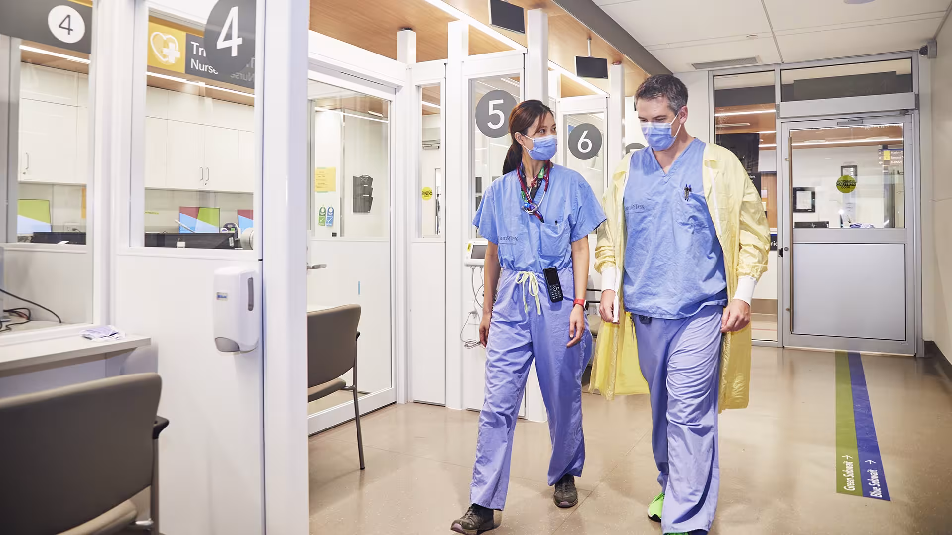 Two doctors in scrubs, walking side by side down the hallway of the Emergency Centre.