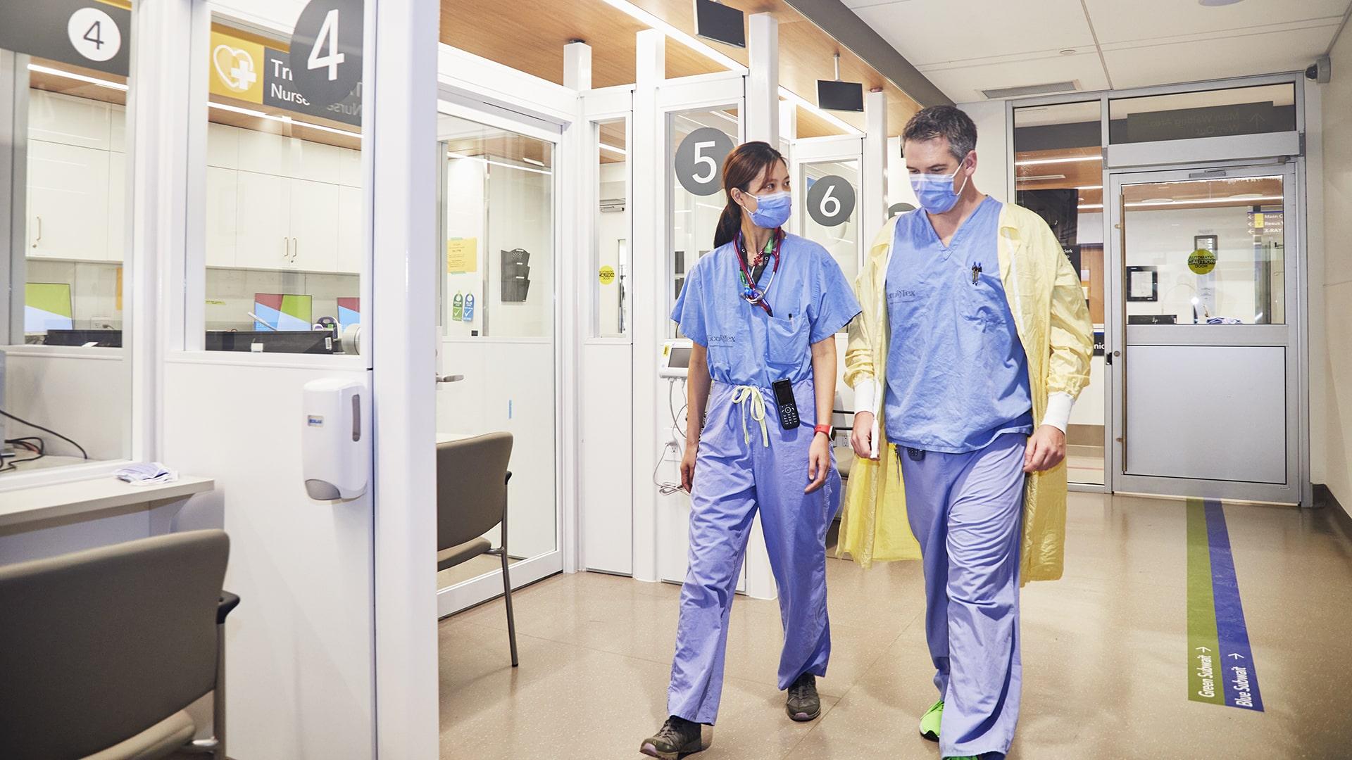 Two doctors in scrubs, walking side by side down the hallway of the Emergency Centre.