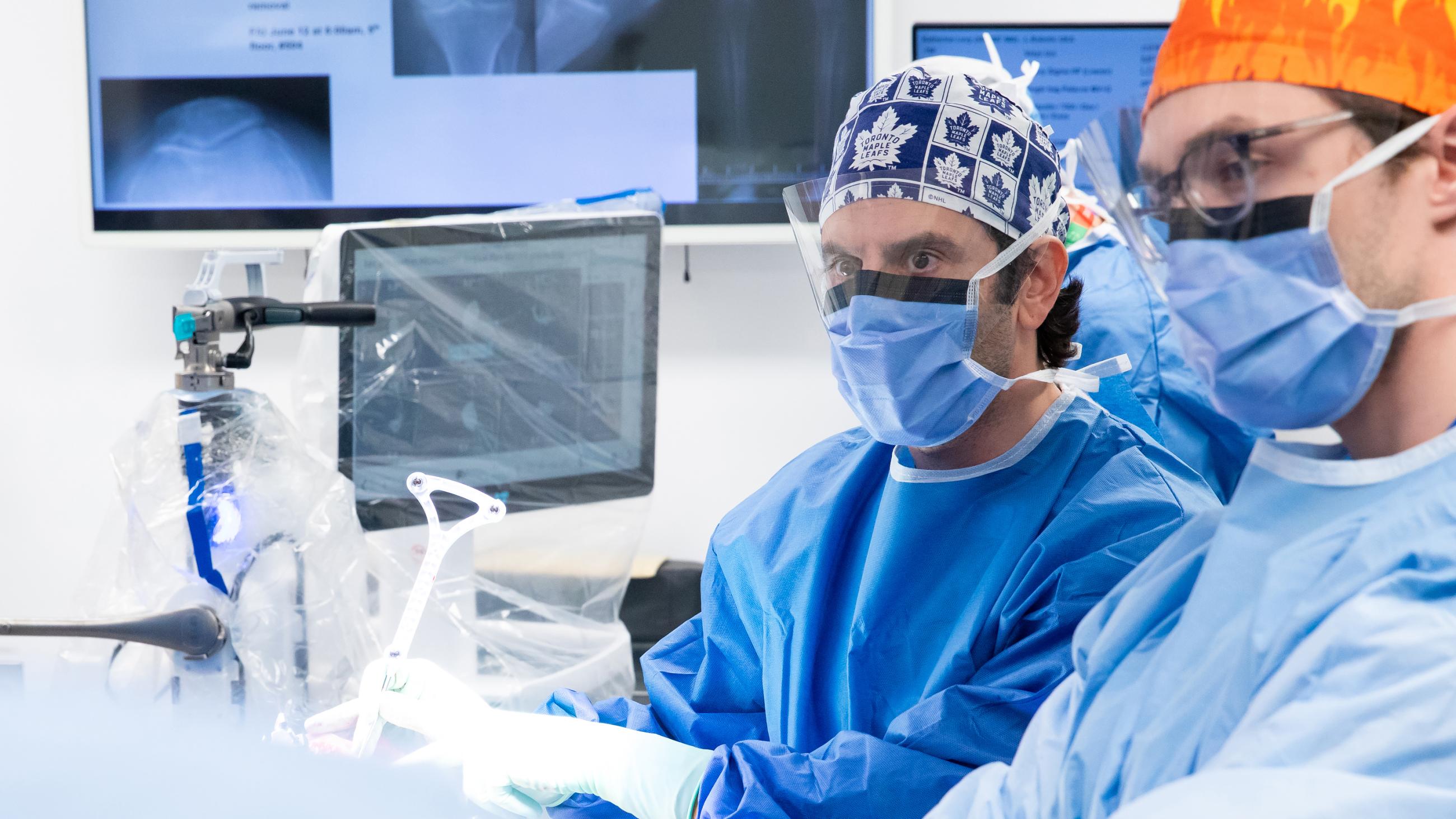 Dr. Jesse Wolfstadt in a blue gown and mask using advanced robotic equipment in a sterile operating room.