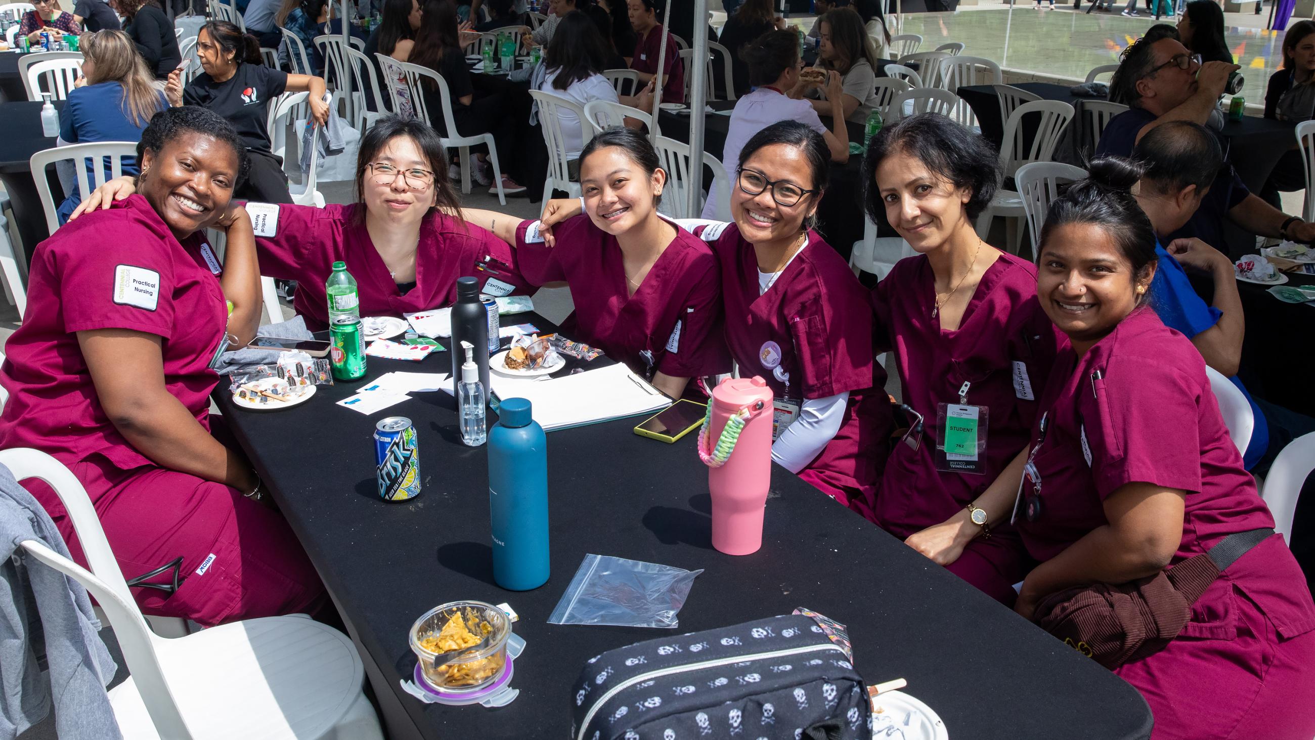A group of six hospital workers smiling and sitting together around a table at the barbeque.
