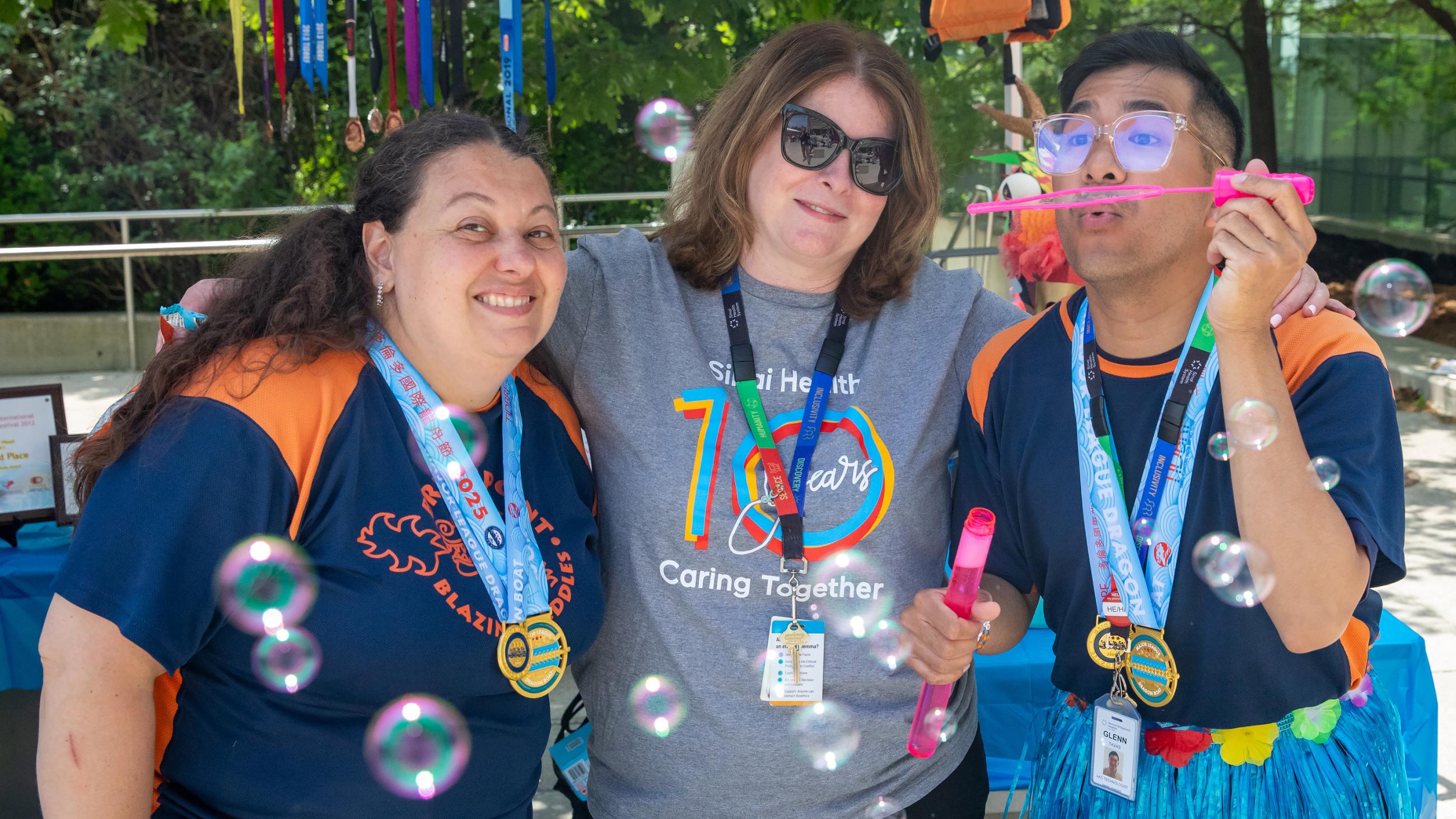 Two colleagues smiling and posing with a third colleague blowing bubbles. 