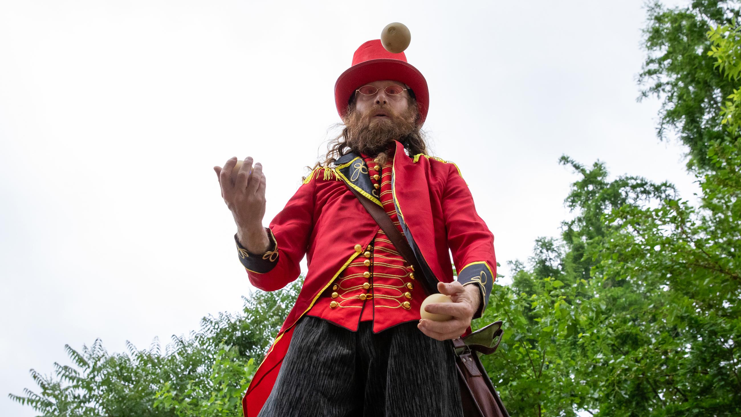 A circus performer juggling while walking on stilts. 