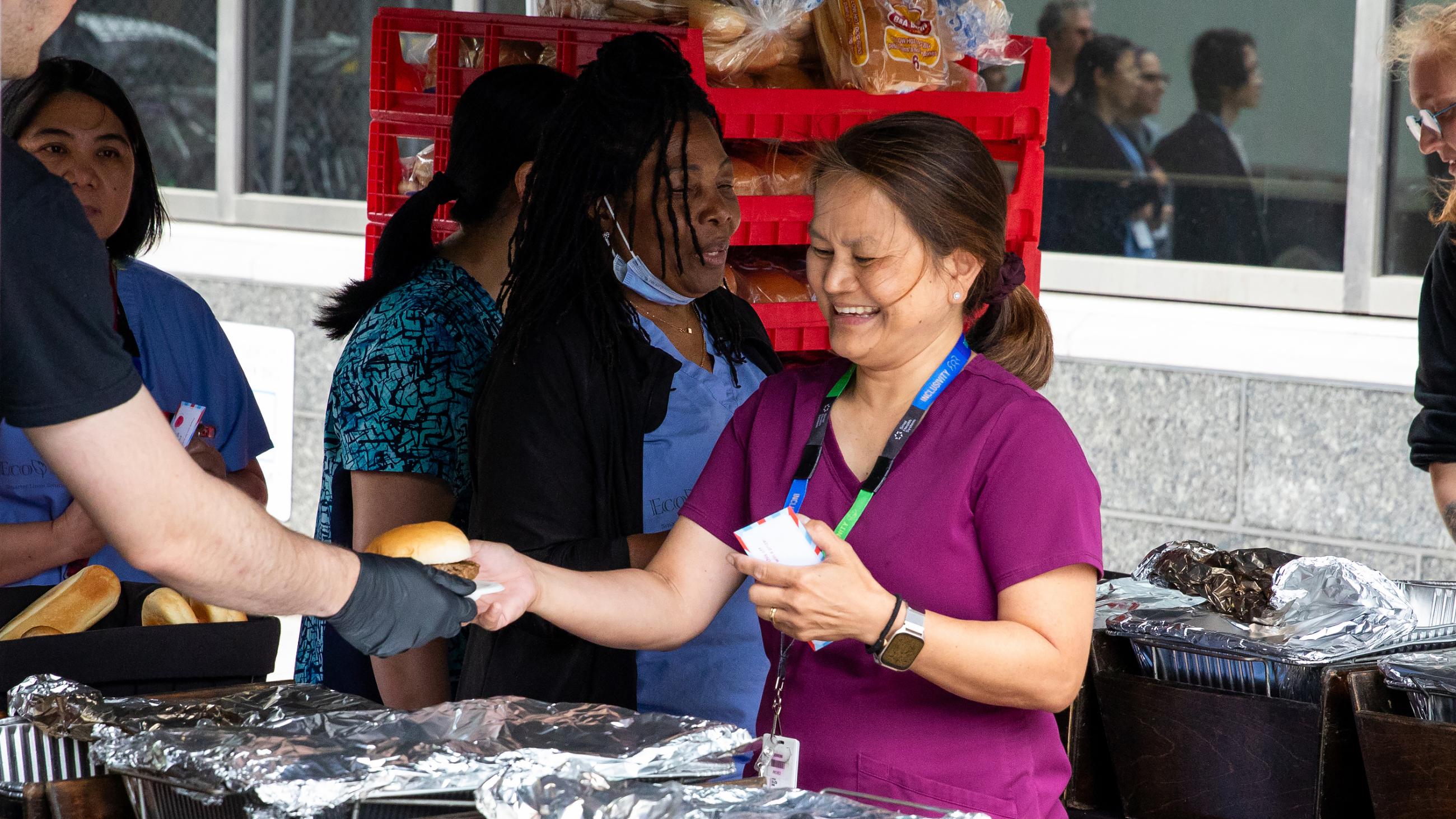 A hospital worker receiving a hamburger at the barbeque. 