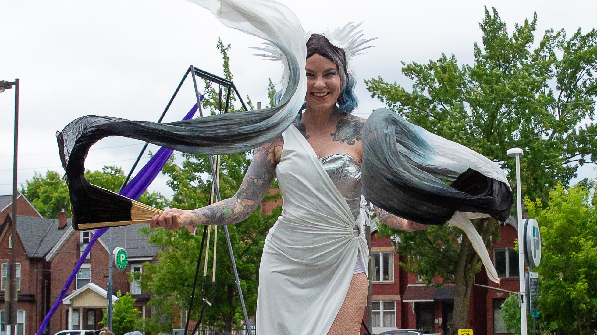 A circus performer waving flags while walking on stilts. 