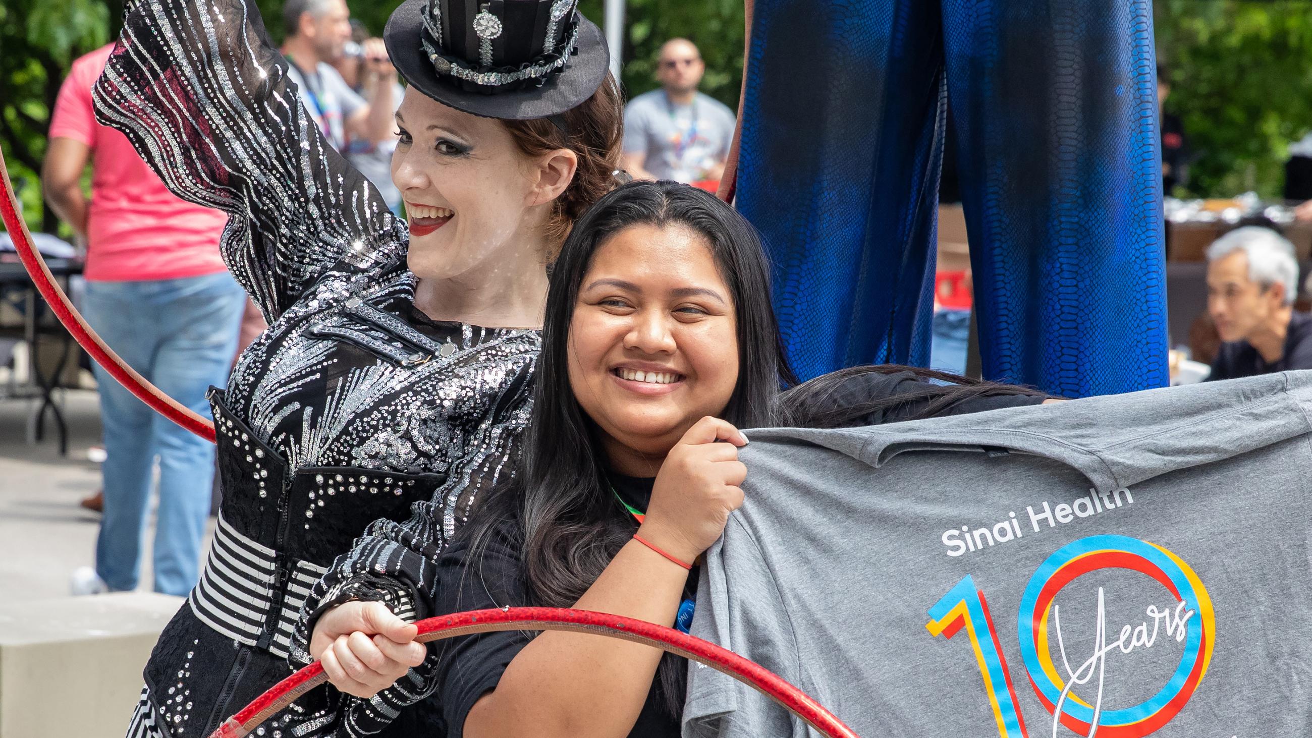 A circus performer with hula hoops posing next to a hospital worker holding up a Sinai Health t-shirt.
