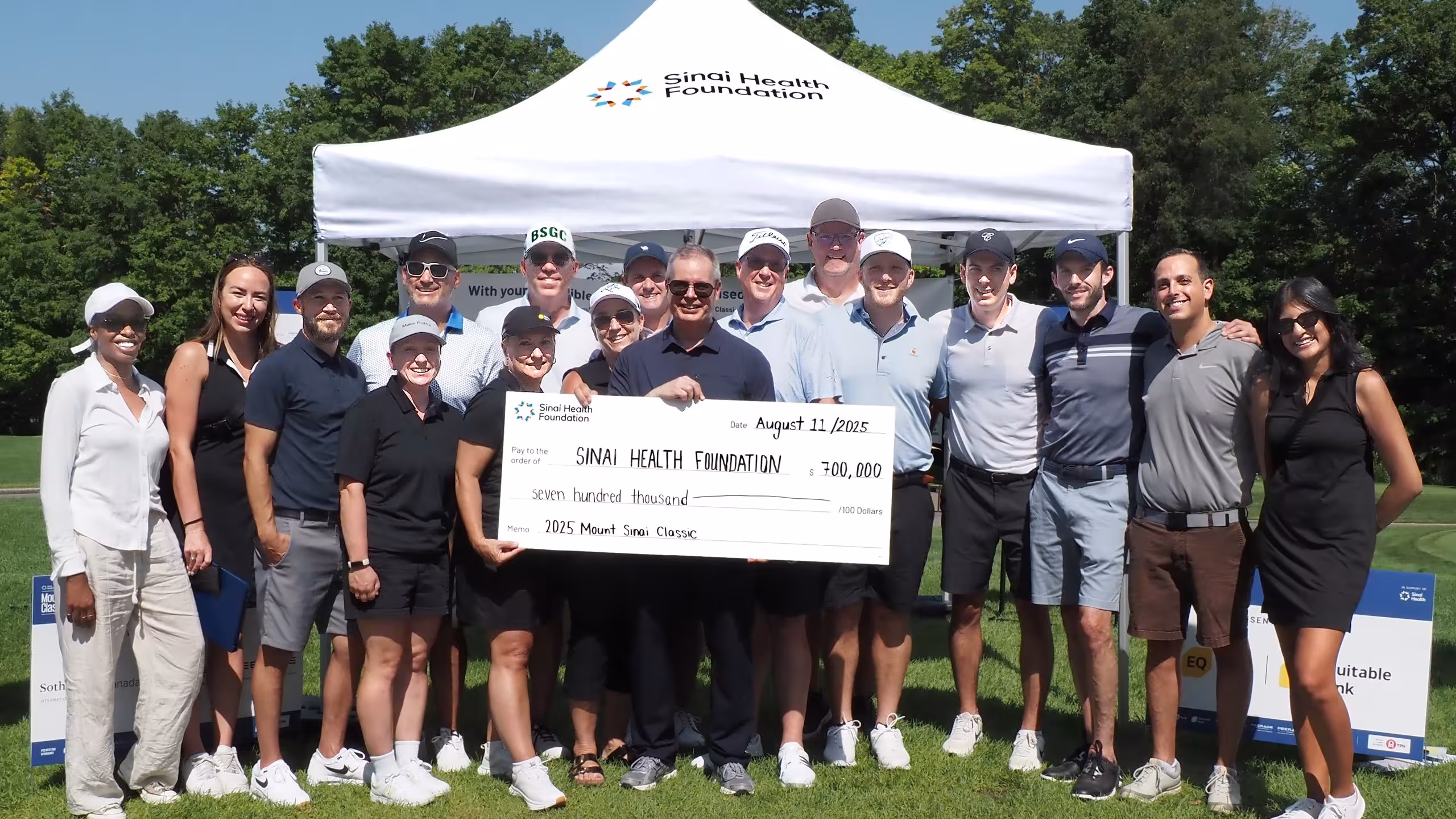 group stands outside holding presentation cheque