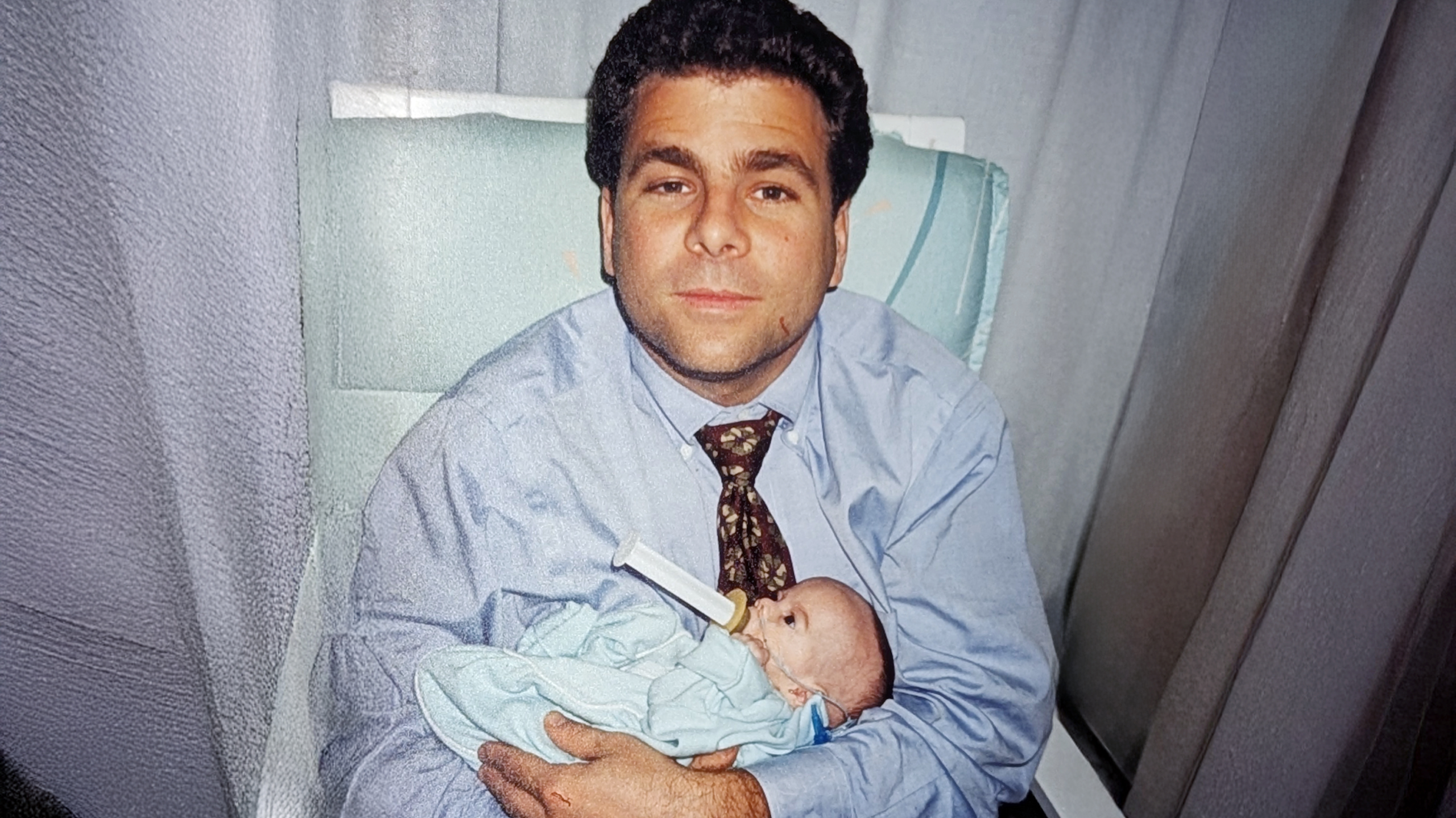 man sits in hospital holding infant