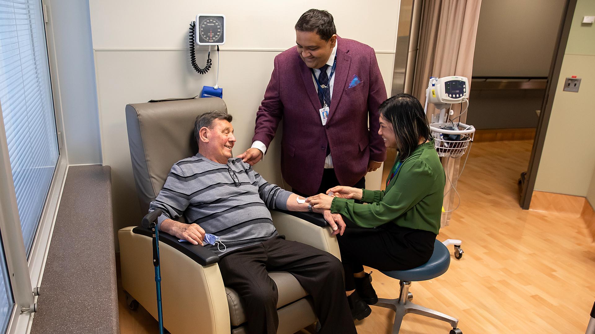 A patient sitting in a chair receiving an infusion with his care team standing beside him.