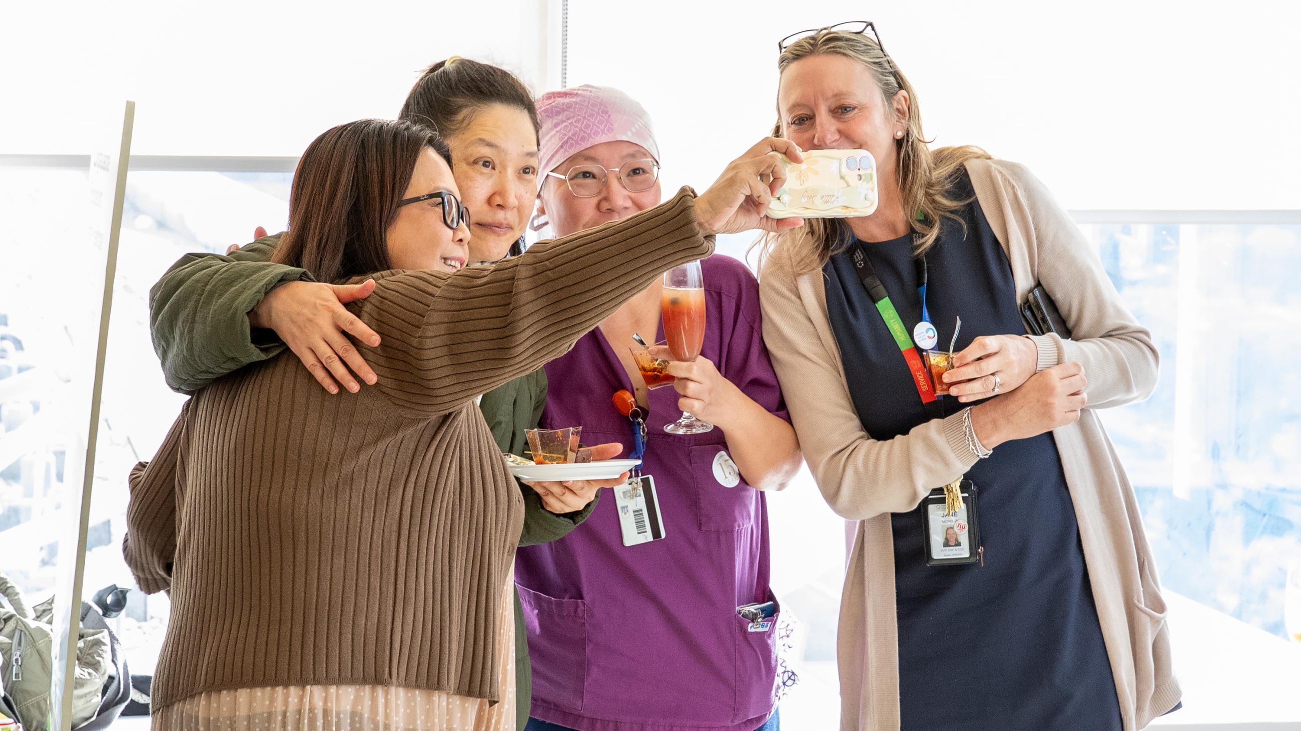 Four people smiling and posting together while taking a selfie.