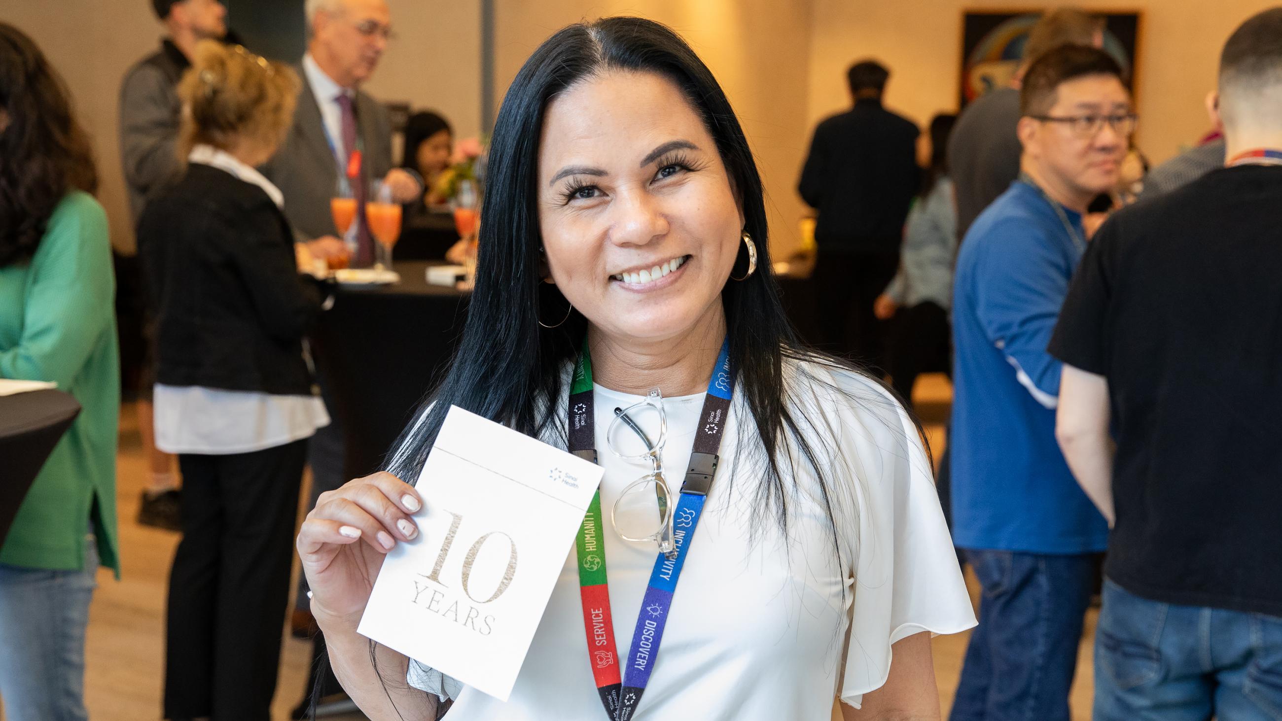 Service milestone recipient smiling while proudly holding up their 10-year invitation card.