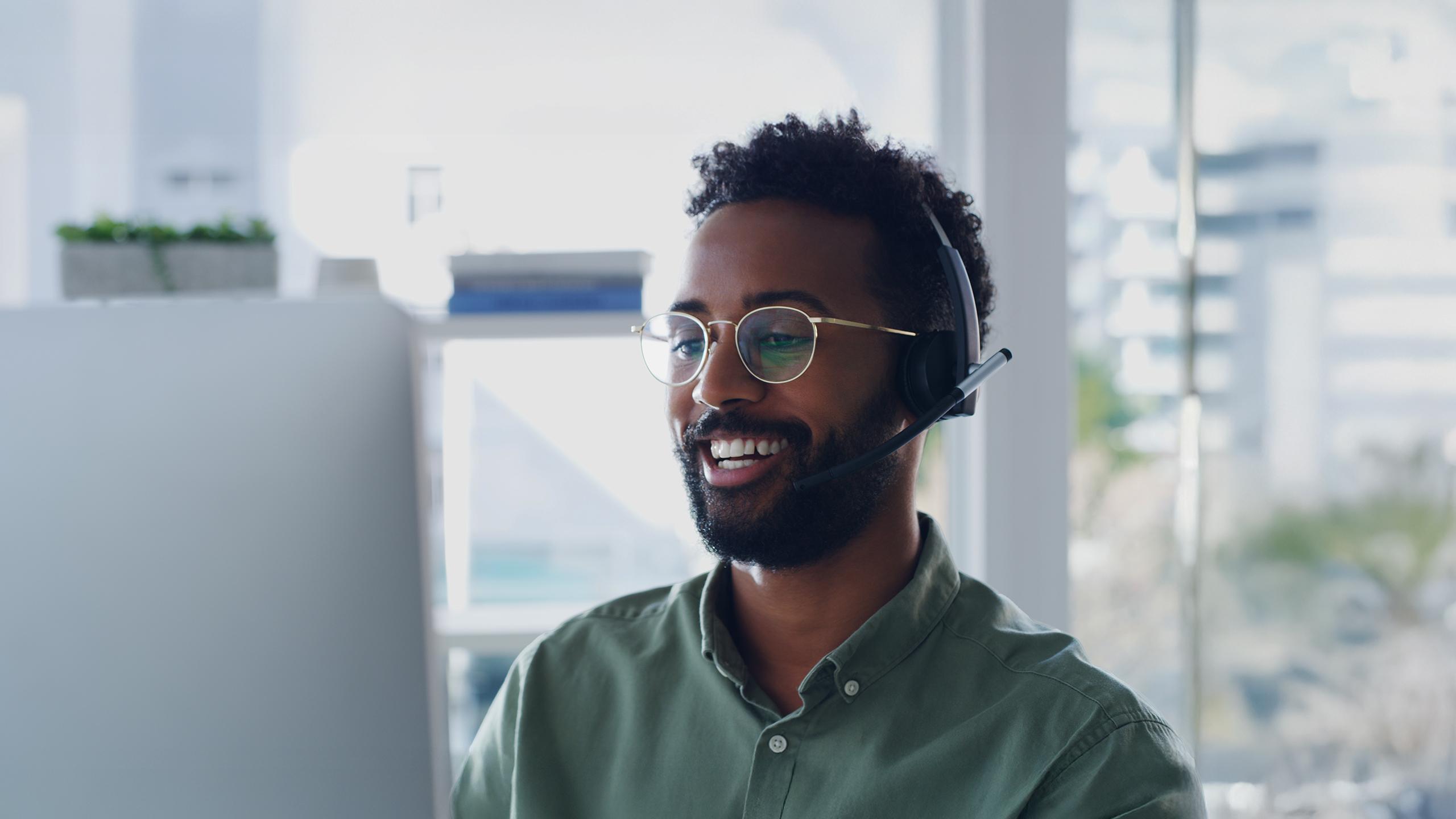 Male telemarketer speaking to customer on a headset while looking at a computer screen