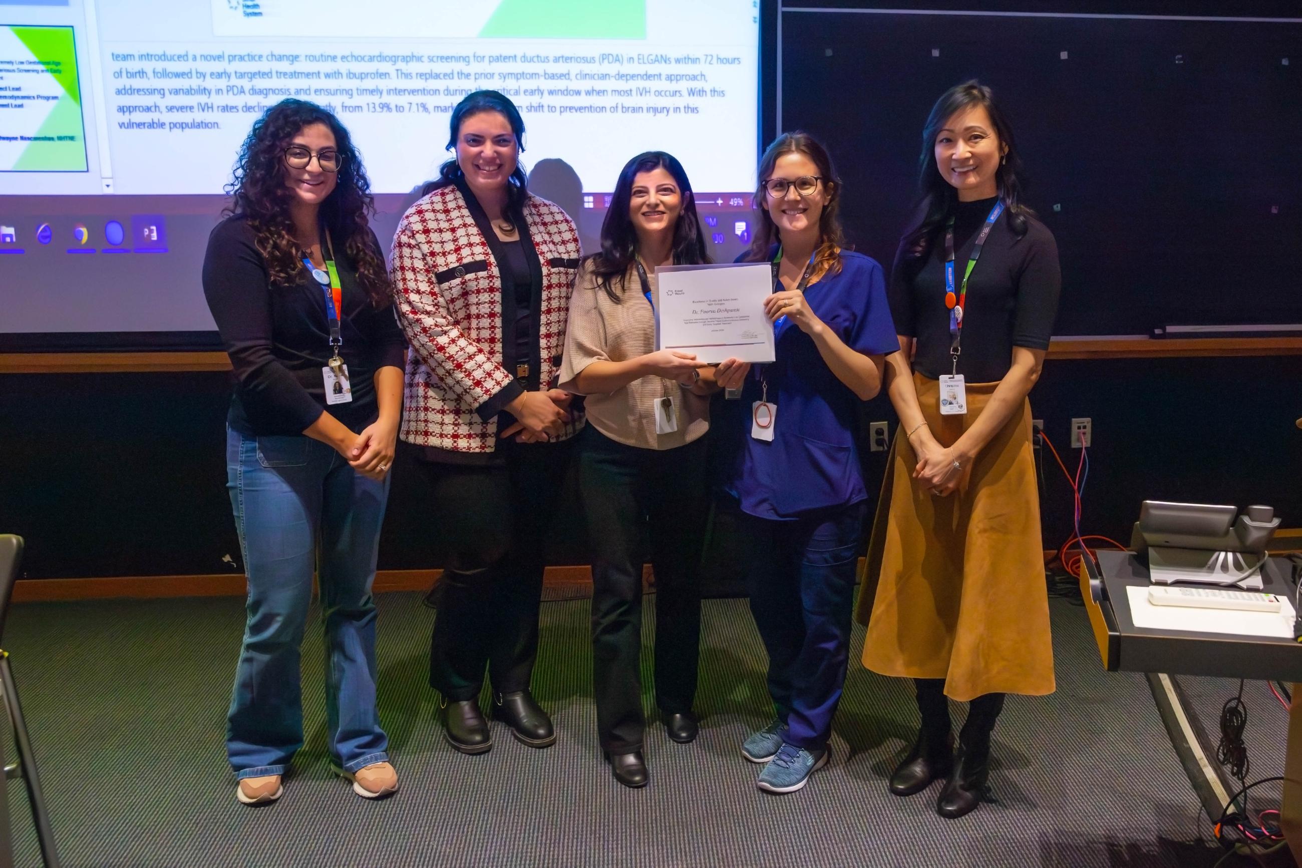 People stand in a line side-by-side, looking at the camera smiling. Some are holding certificates they have been awarded.