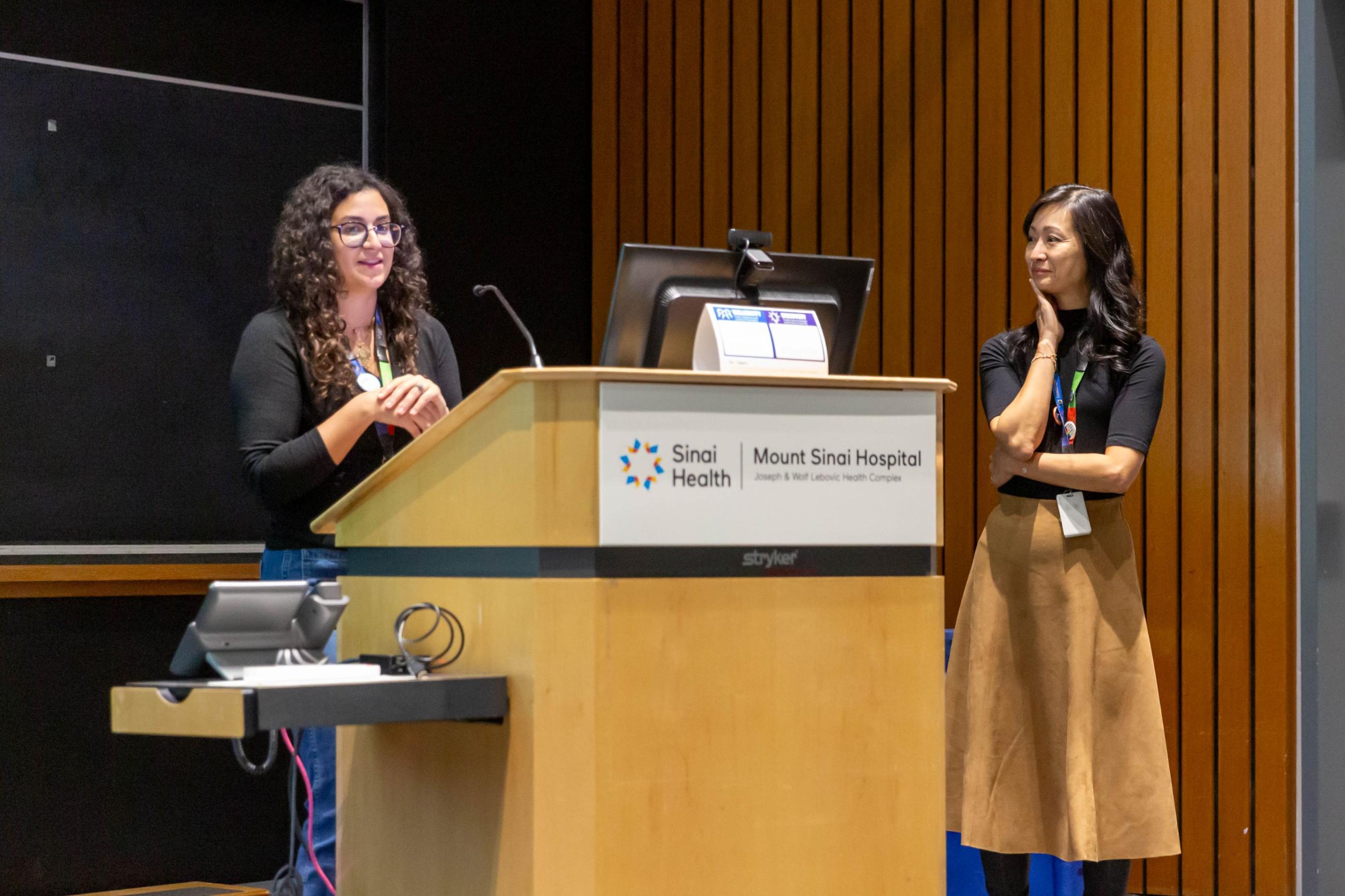 A woman stands at a podium in an auditorium giving a presentation