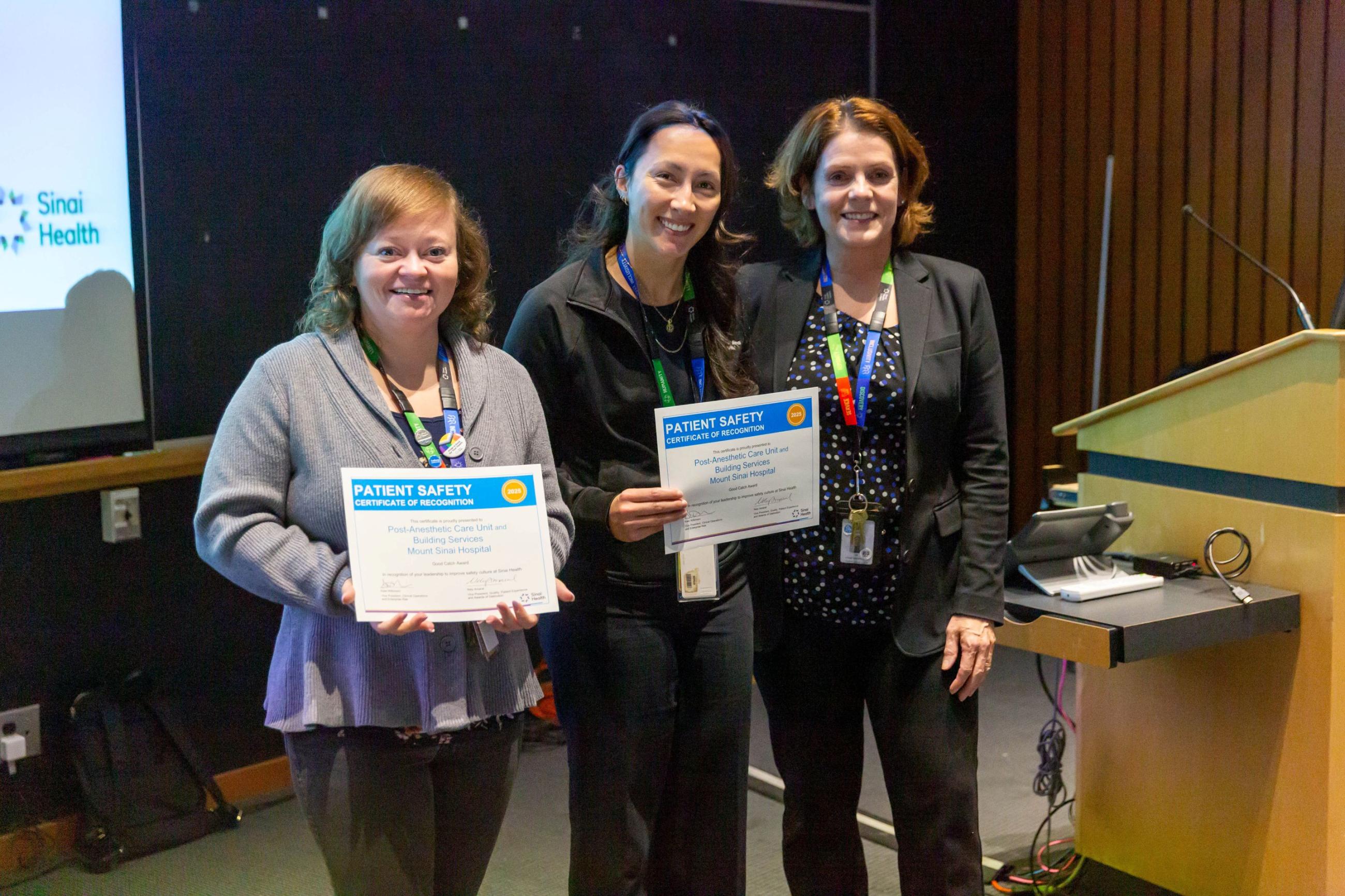 A group of three people stand side-by-side following an awards presentation. They are looking at the camera smiling. Two are holding certificates.