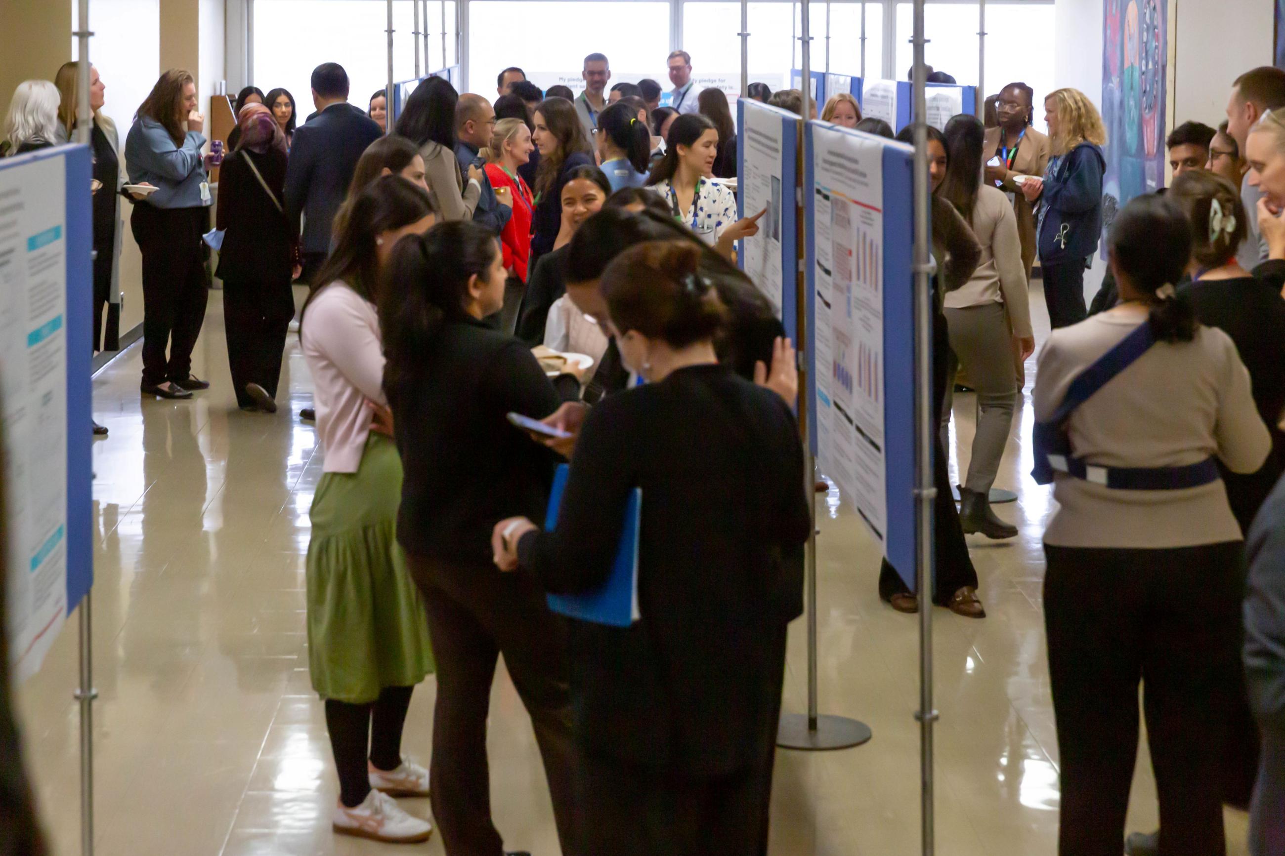 A room with a crowd of people looking at scientific posters on display boards.