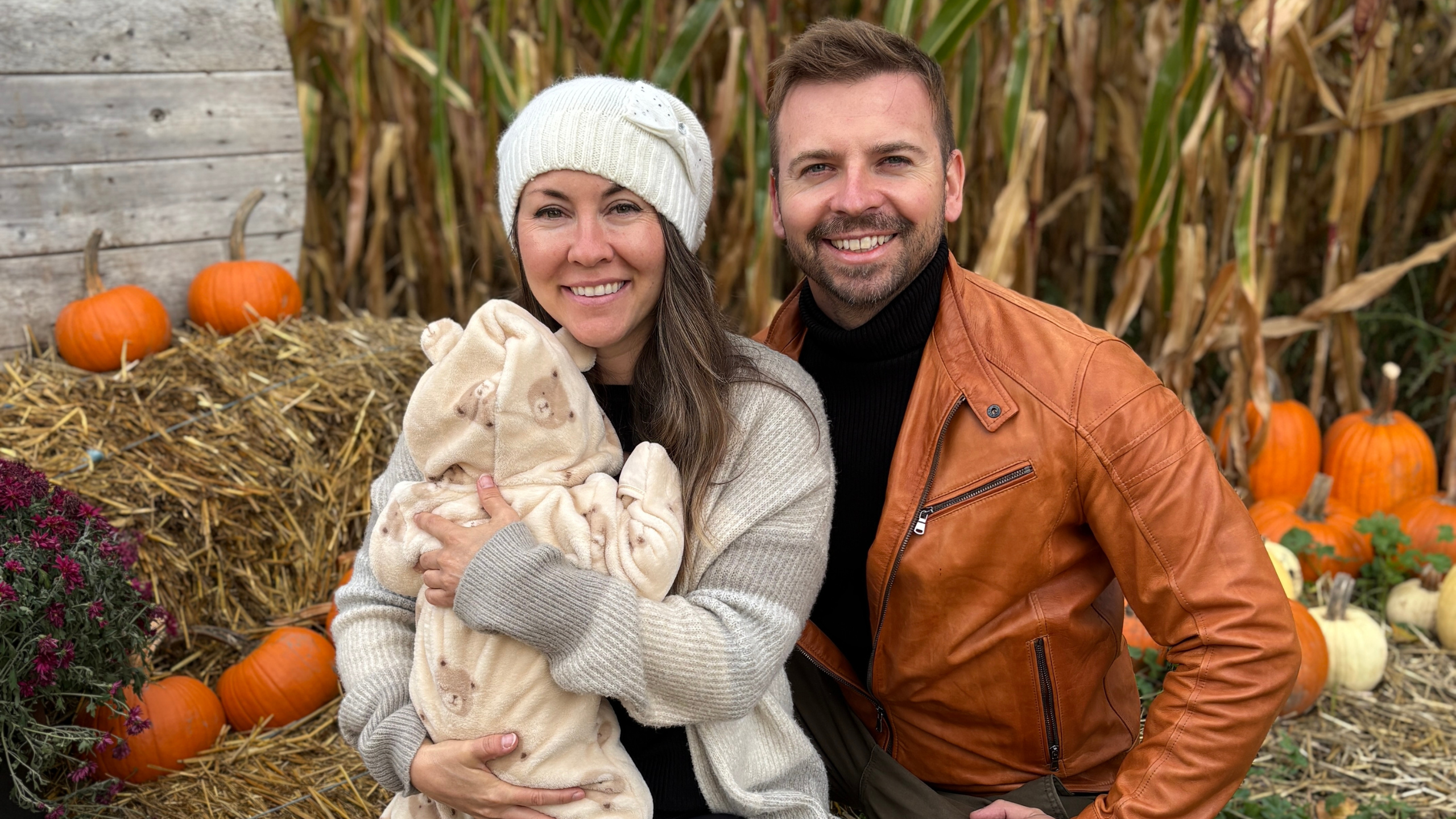 woman holding baby sits next to a man in against a fall backdrop