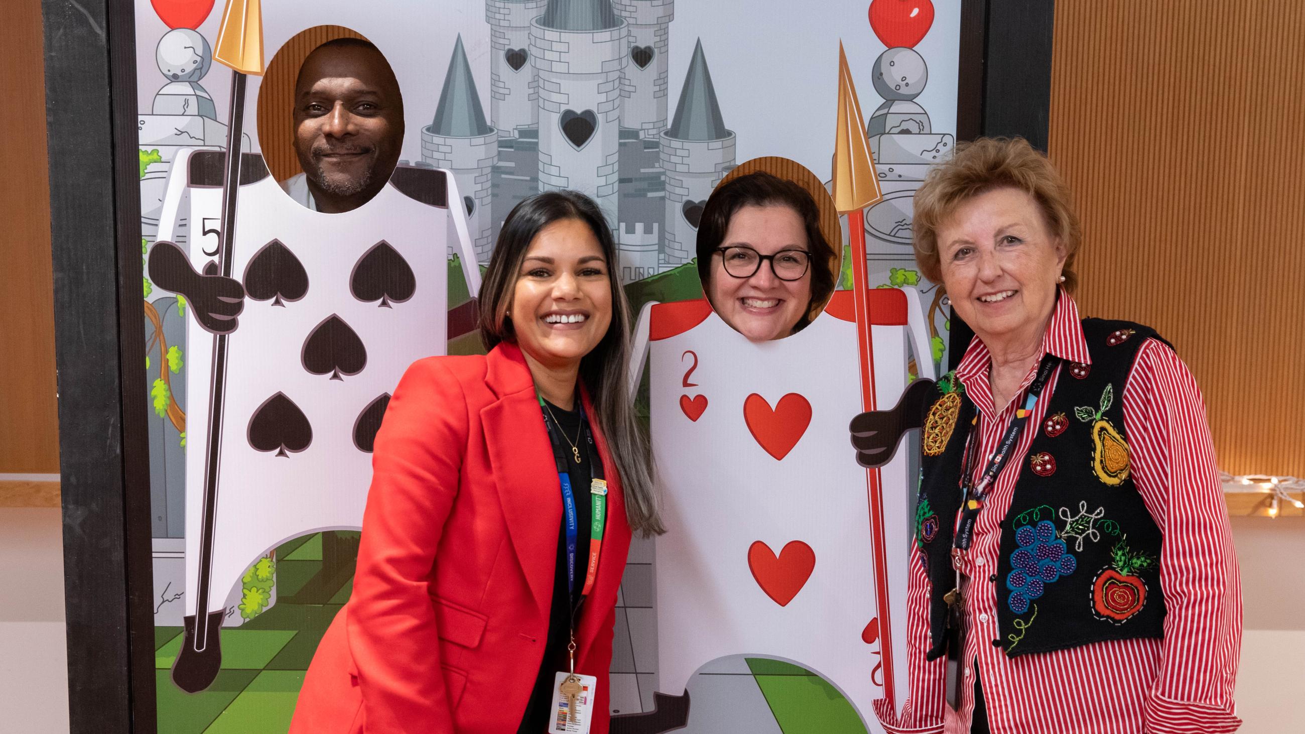 People smiling and posing behind and in front of a photo stand-in featuring card-soldiers from Alice in Wonderland.