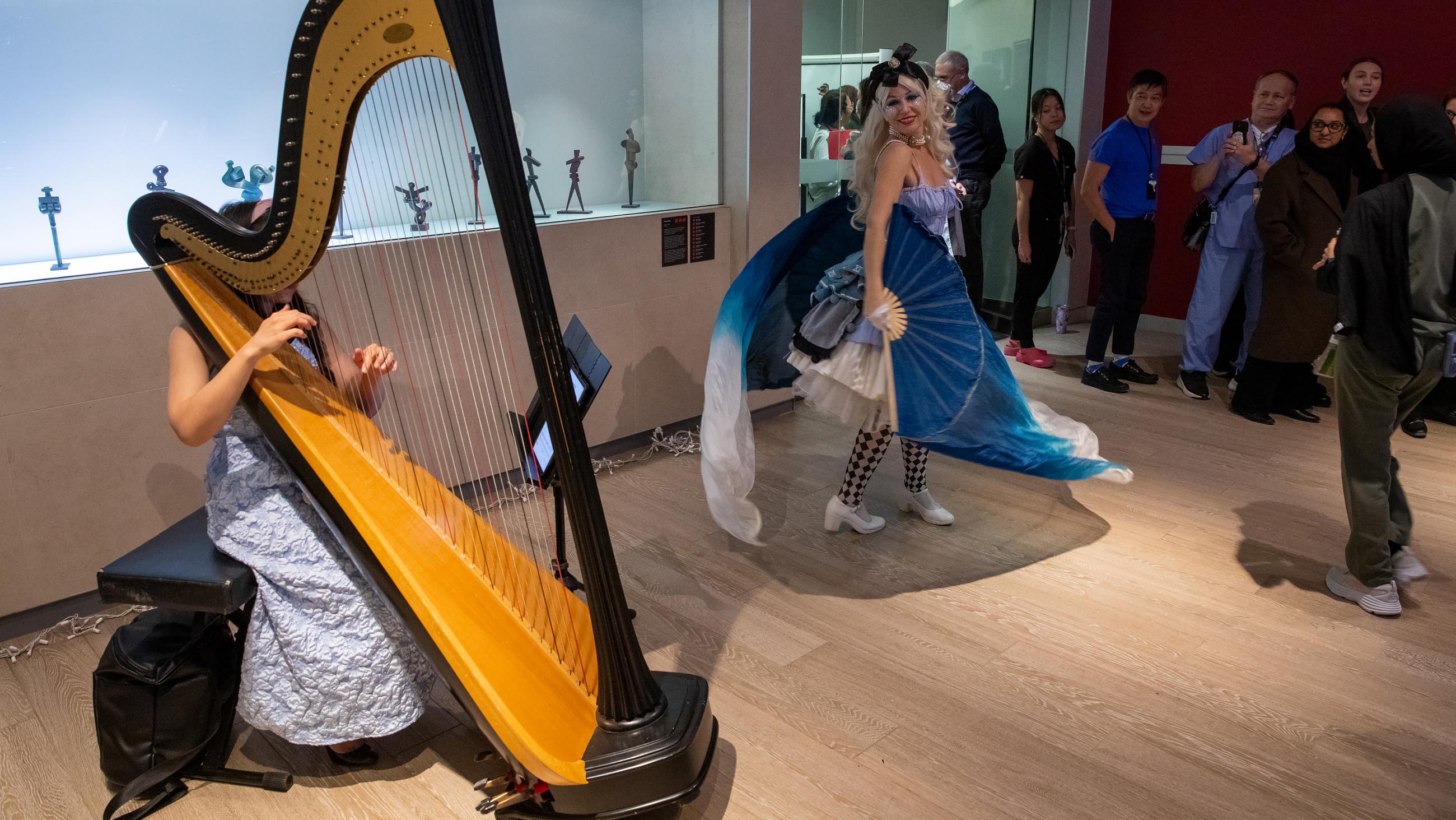 A musician playing the harp as an Alice in Wonderland performer entertains the crowd during the open house.