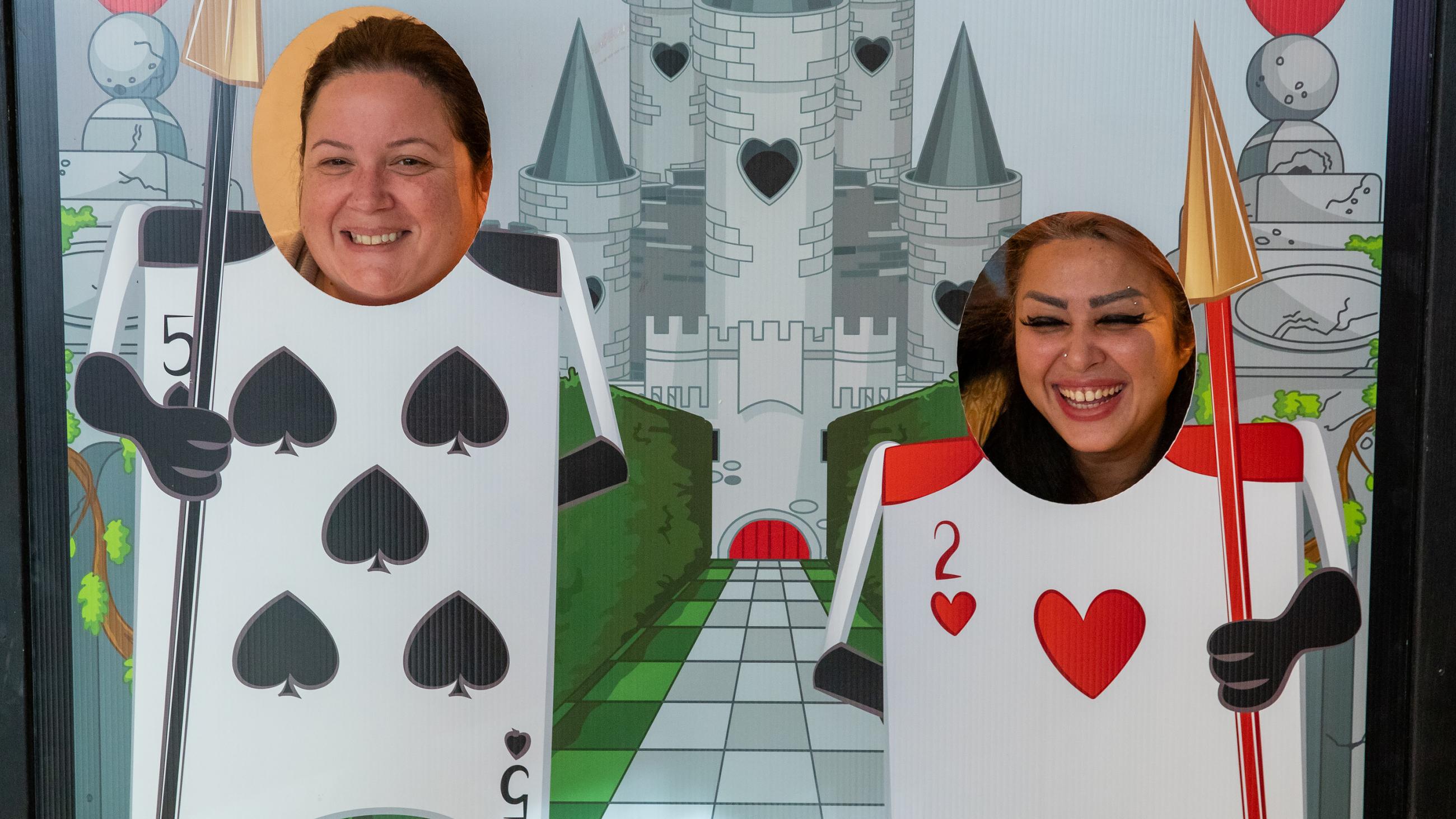 Two people smiling and posing behind a photo stand-in featuring card-soldiers from Alice in Wonderland.