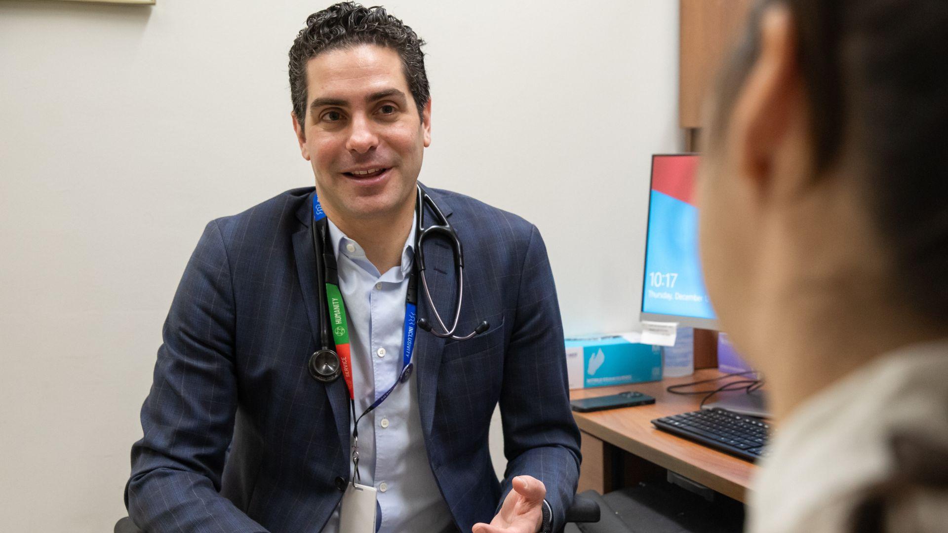 Dr. Nathan Stall, Geriatritician, Clinician Scientist and Geriatrics Site Lead at Sinai Health, sits with a patient in an exam room at Mount Sinai Hospital.