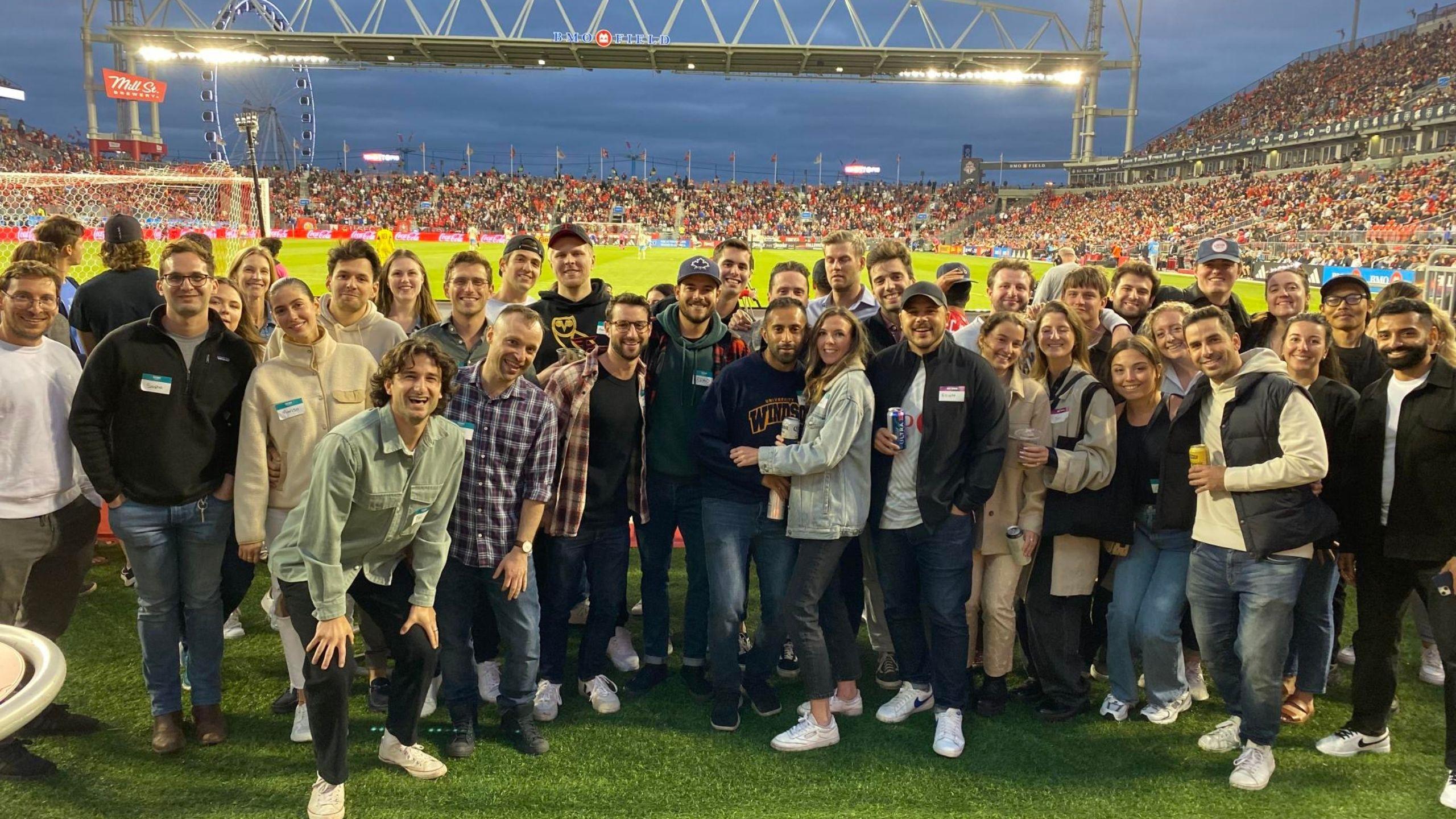 A crowd of approximately 35 guests standing and posing on the field at BMO Field, smiling while attending soccer game event