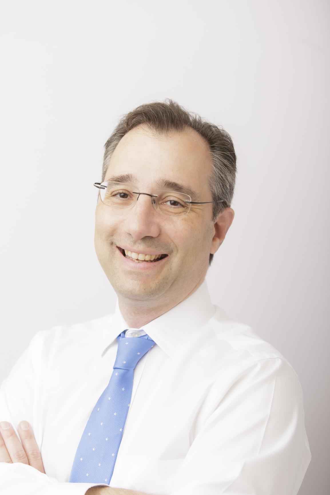Dr. David Gratzer, head and shoulders portrait. He is looking at the camera smiling and wearing a white shirt with a blue tie