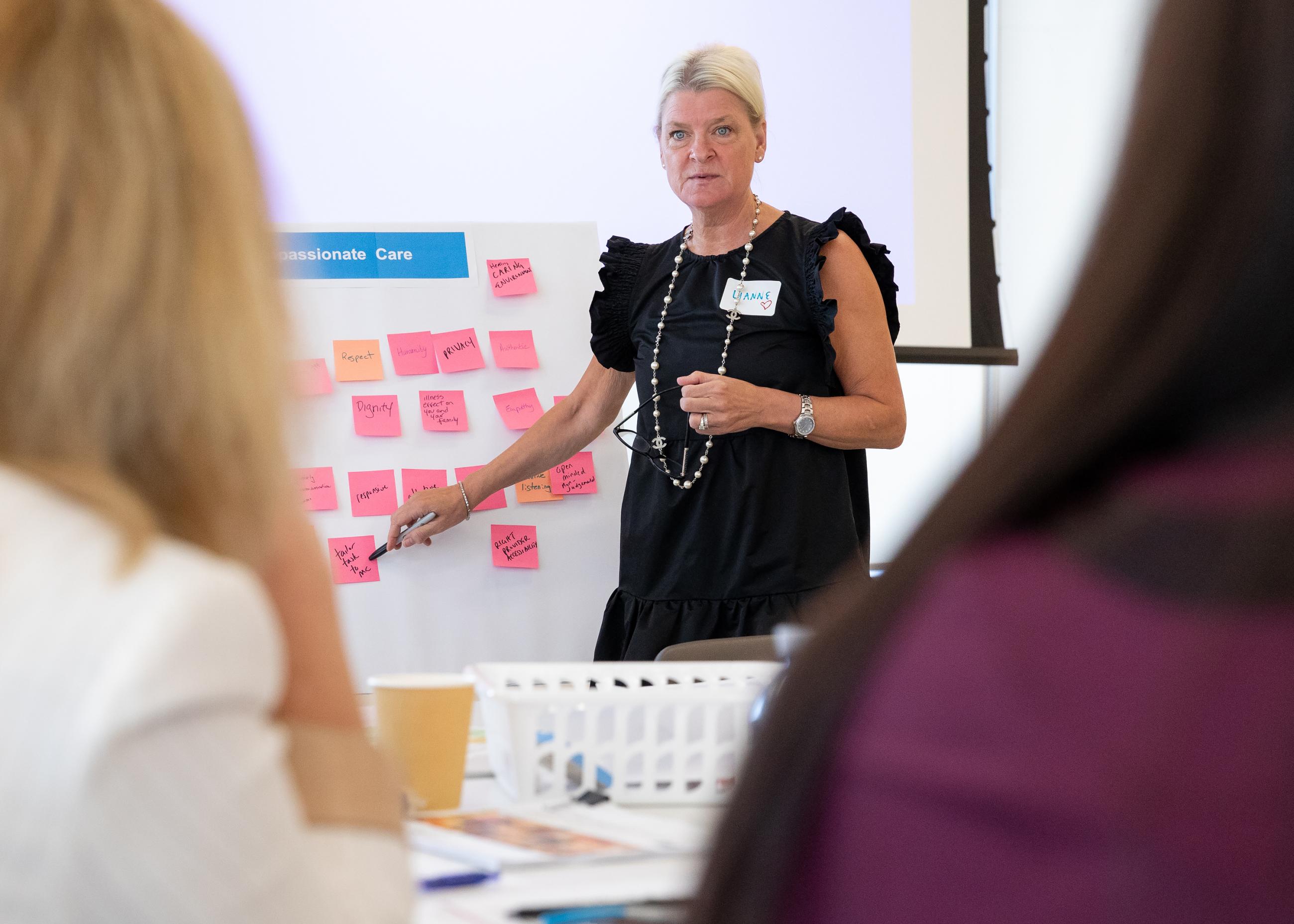 Dr. Lianne Jeffs pointing to a whiteboard with compassionate care descriptors during a presentation. 