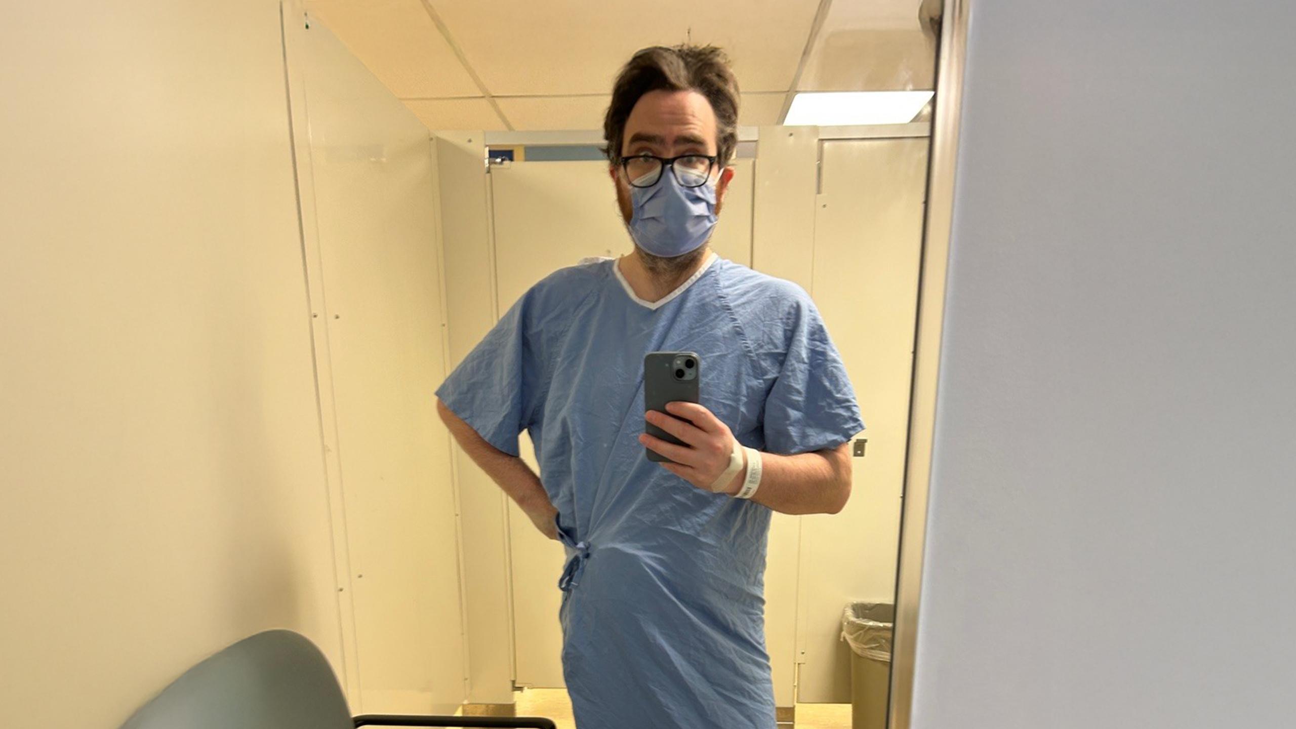Man wearing hospital gown stands in bathroom