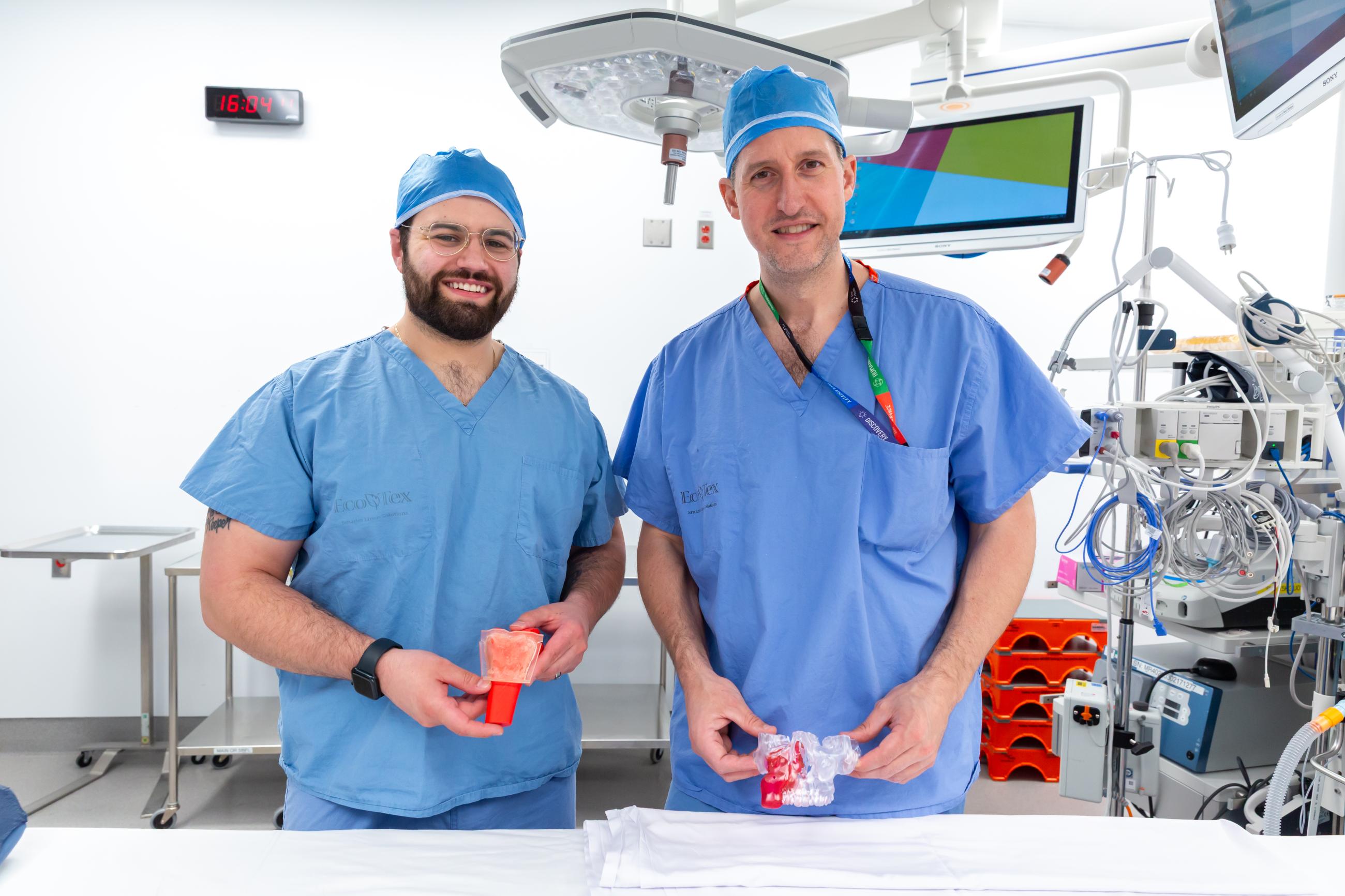 Qwynn  Ferreira and Dr. Joel Davies smiling and standing in an operating room holding the 3D models used in surgery.