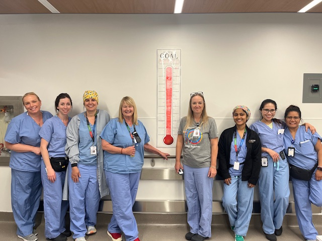 A group of staff members from the Peri-operative services team smile beside a poster showing their recycling goals have been met.