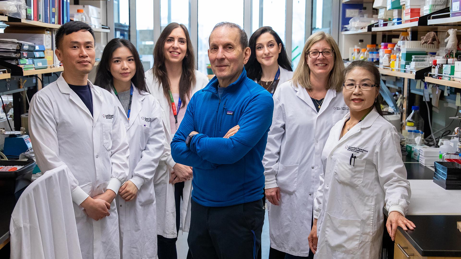 Dr. Daniel Drucker posing in the center with his lab members on each side of him in their lab.