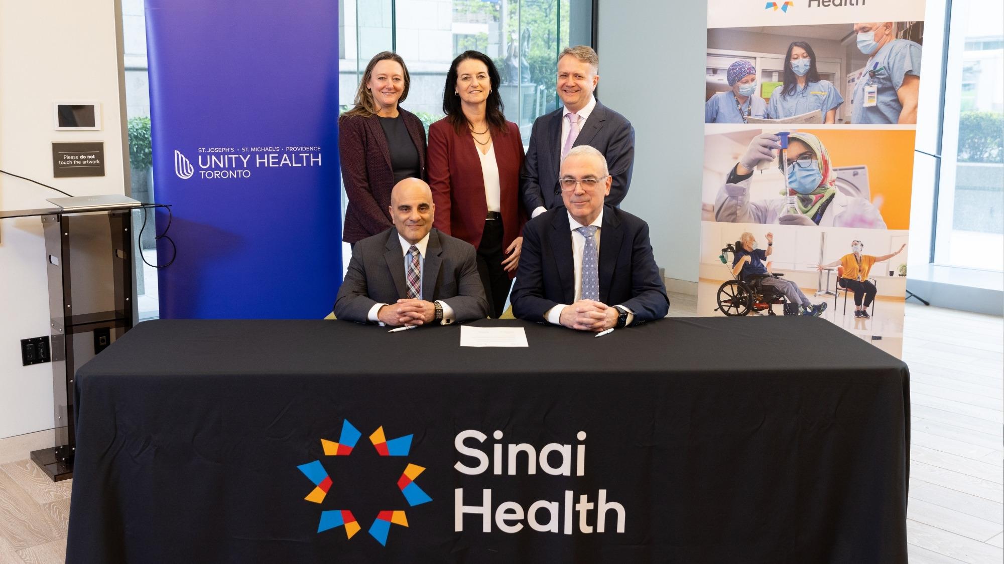 Members of hospital leadership posing in front of Sinai Health and Unity Health Toronto banners.