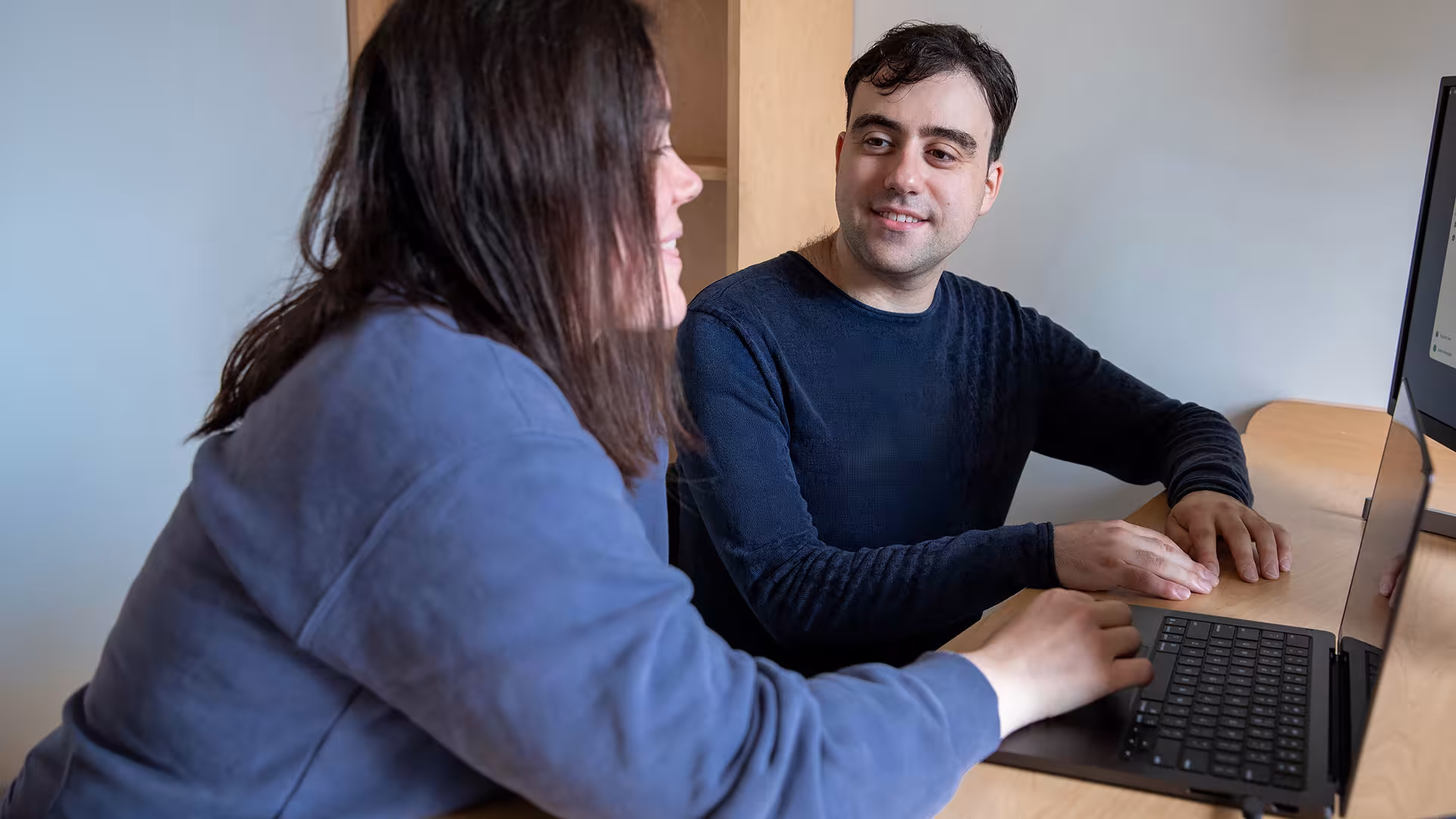 Dr. Michael Wainberg smiling at Isabel Kerrebijn, sitting at a desk beside one another with an open laptop in front of them. 