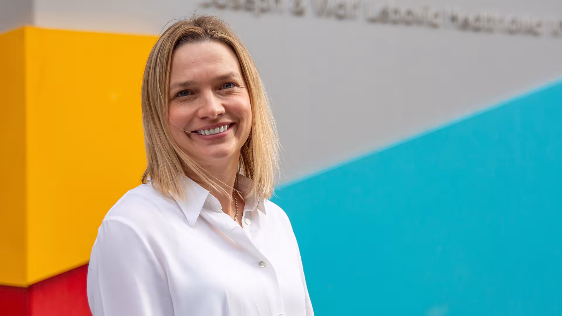 Dr. Jennie Johnstone smiling with a bright background coloured orange, blue and red for the Sinai Health branded colours. 