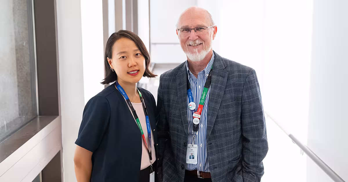 Two people in a brightly lit hallway standing beside each other smiling.