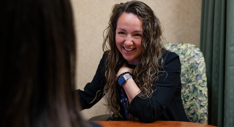 Dr. Amanda Steiman sits at a desk across from another woman who's back is to the camera and shoulder is in the frame. Dr. Steiman is smiling and interacting with the woman