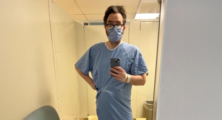 Man wearing hospital gown stands in bathroom