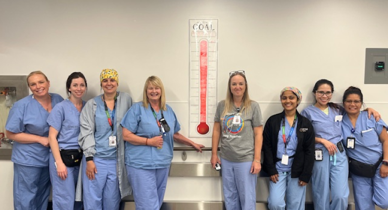 A group of staff members from the Peri-operative services team smile beside a poster showing their recycling goals have been met.
