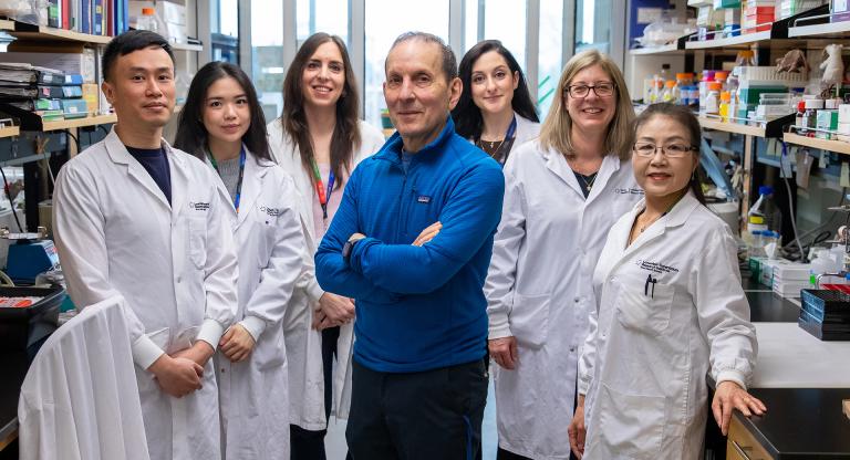Dr. Daniel Drucker posing in the center with his lab members on each side of him in their lab.