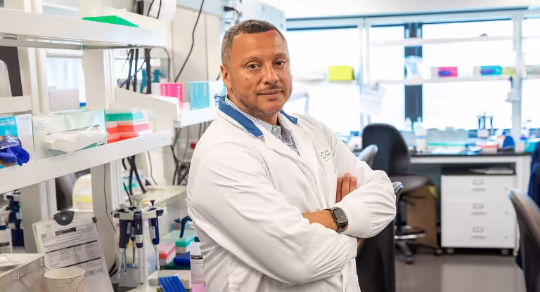 Dr. George Charames in a white lab coat standing in a laboratory.