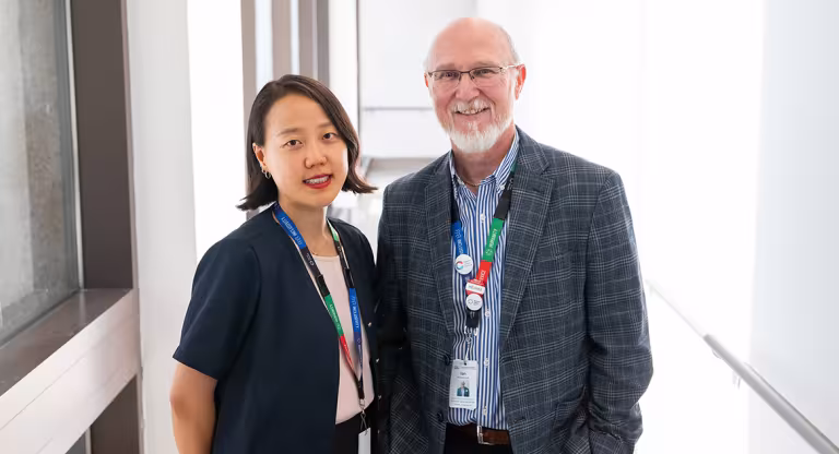 Two people in a brightly lit hallway standing beside each other smiling.