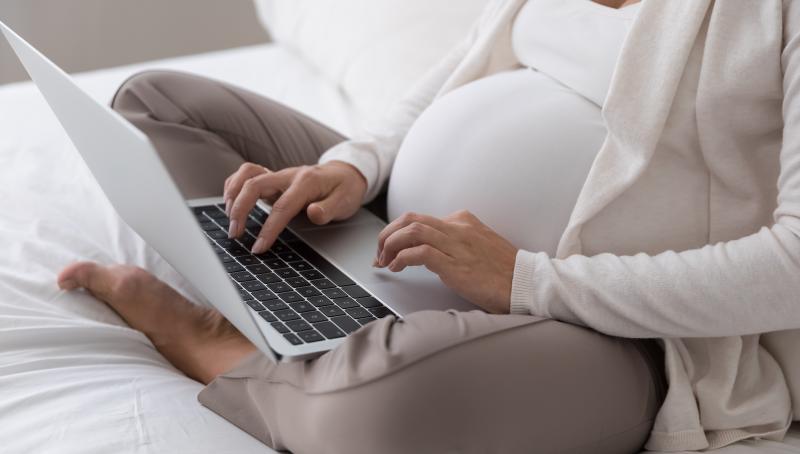 Pregnant woman using a laptop on her lap.