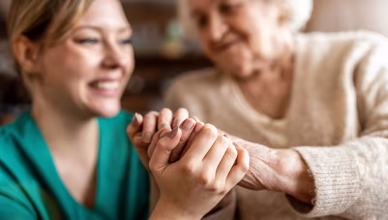 Close-up of a health care worker gently holding the hands of an older adult patient.