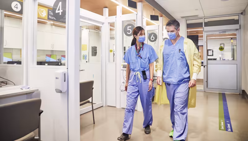 Two doctors in scrubs, walking side by side down the hallway of the Emergency Centre.