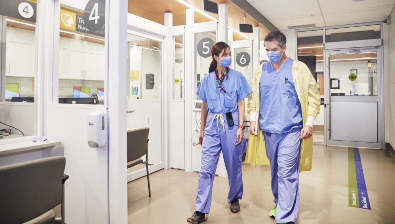 Two doctors in scrubs, walking side by side down the hallway of the Emergency Centre.
