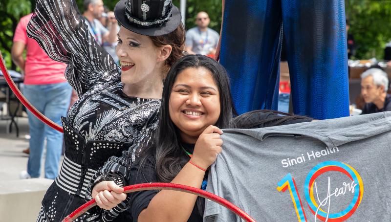 A circus performer with hula hoops posing next to a health-care provider holding up a Sinai Health t-shirt. 