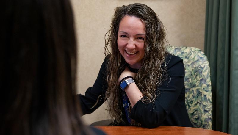 Dr. Amanda Steiman sits at a desk across from another woman who's back is to the camera and shoulder is in the frame. Dr. Steiman is smiling and interacting with the woman