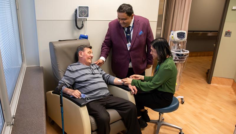 A patient sitting in a chair receiving an infusion with his care team standing beside him.