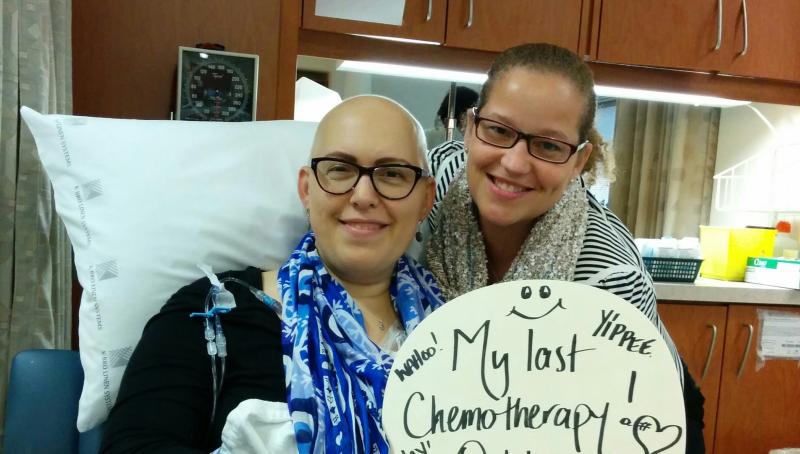 woman sits in hospital bed with sign that says, 'my last chemotherapy'
